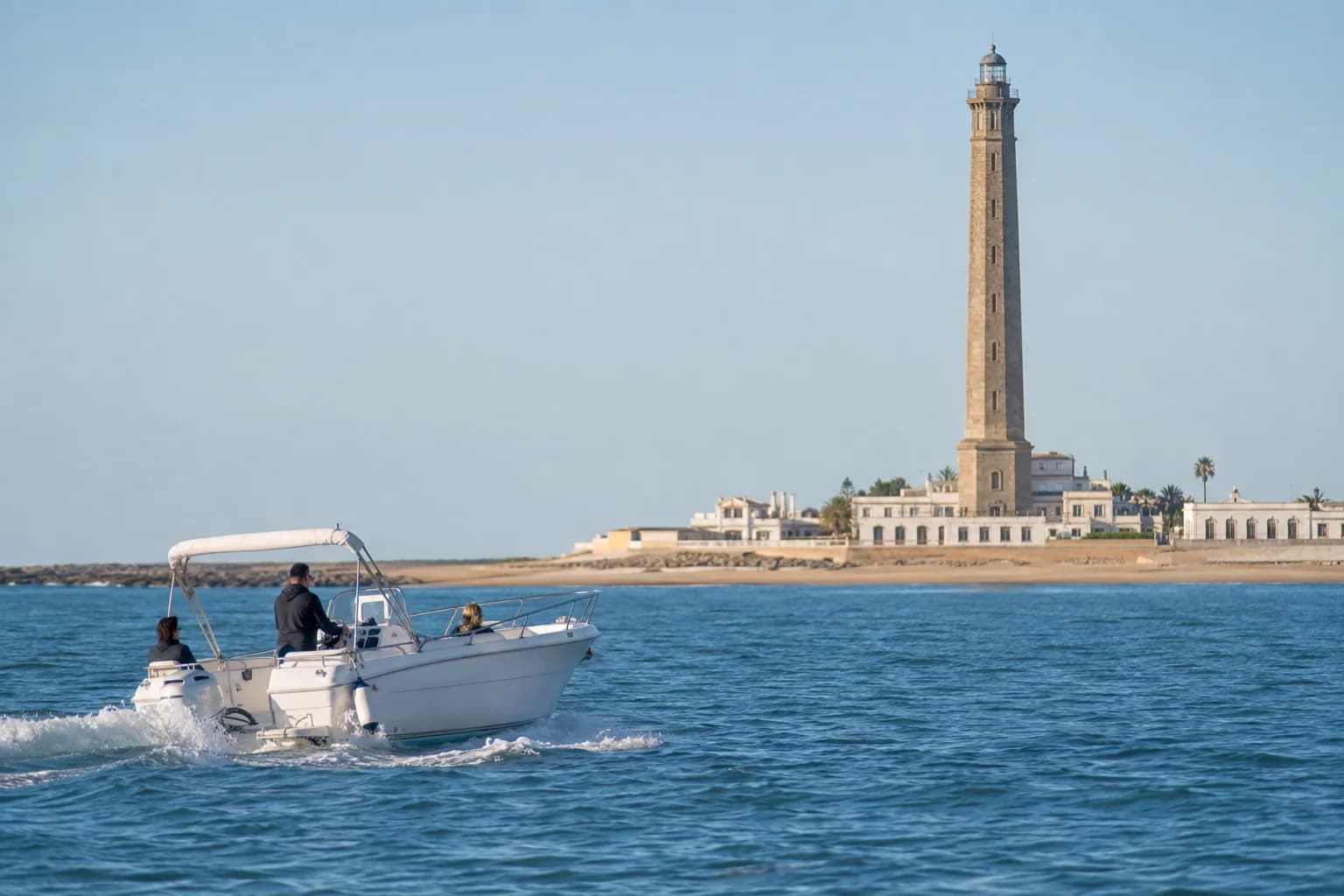 Barco navegando frente al faro y la costa de Chipiona