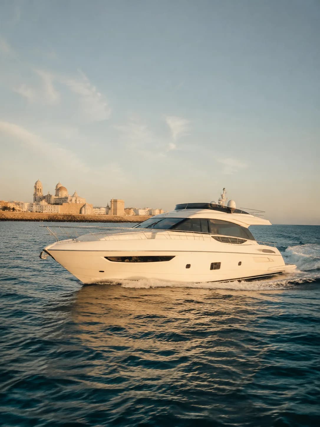 Yate blanco contemporáneo navegando frente a la costa de Cádiz al final de la tarde